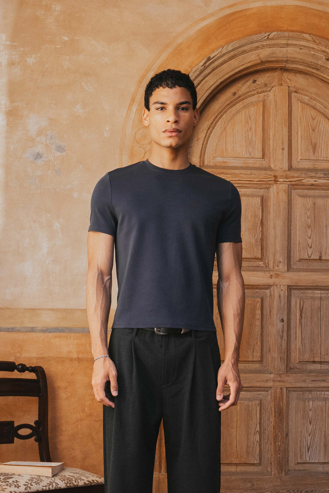Man wearing a black t-shirt and pants standing in front of a wooden door.