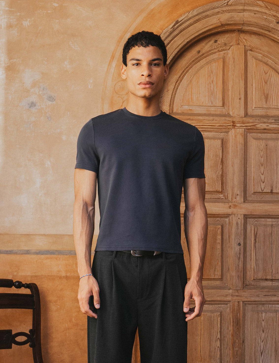 Man wearing a black t-shirt and pants standing in front of a wooden door.