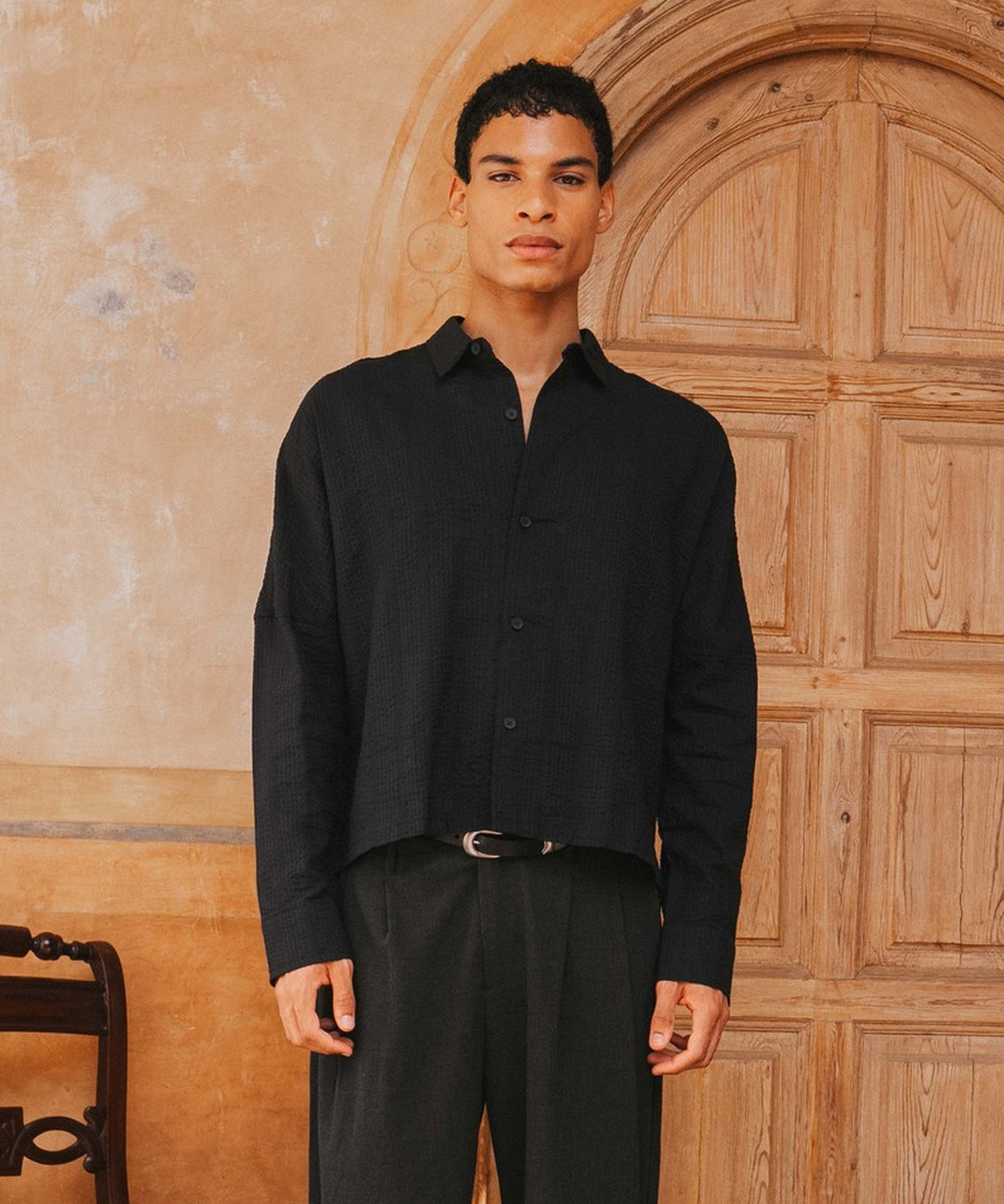 Man wearing a black shirt and pants standing in front of a wooden door.